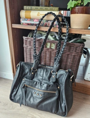 Svart handväska - På framsidan finns ett fack med dragkedja och ett fack med magnetlås. På baksidan finns ytterligare ett fack med dragkedja. Inuti väskan, som stängs med dragkedja, finns ett mindre dragkedjefack och två små fack för sånt som annars lätt försvinner i väskan.  Jag har sytt fast en av remmarna i väskan, då den börjat lossa från ena fästet. Detta är varför de finns stygn på insidan. Detta påverkar inte funktionen. Kom privat för mått!