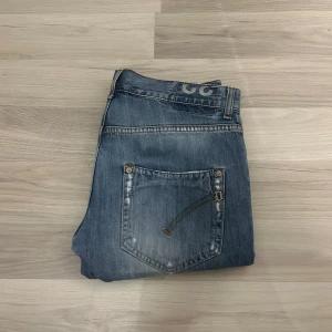 2 Dondup jeans - Säljer två par jeans från LC med snygg broderad detalj på bakfickan. Ena paret är ljusblå med slitningar och den andra är mörkblå med kontrastsömmar. Båda har klassisk femficksdesign och raka ben. Perfekt för dig som gillar stilrena jeans med lite edge.