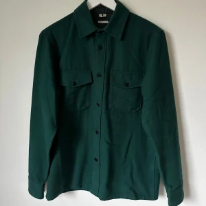Mörkgrön overshirt från Arket - Snygg mörkgrön overshirt från Arket i ullblandad twill. Regular fit med klassisk krage, två stora bröstfickor med knappar och långa ärmar med manschett. Perfekt lager-på-lager-plagg med stilren look och rejäla detaljer. 4A9