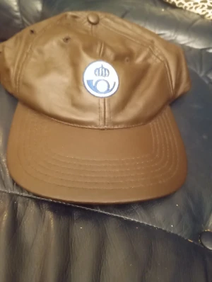 Posten keps läderlook med broderad logga - Snygg brun Posten keps läderlook  Klassisk form med böjd skärm och ventilerande hål. Perfekt för dig som vill sticka ut med en unik accessoar.