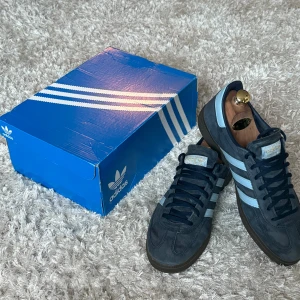 Adidas Spezial mörkblå sneakers - Adidas Spezial sneakers i mörkblå mocka med ljusblå ränder på sidorna och guldtext. Klassisk låg modell med rund tå och platt sula. Skorna har snörning och retrovibe, perfekt för dig som gillar stilrena och tidlösa sneakers. Skorna har inga som helst skador.