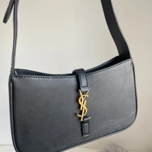 Väska ysl - Svart axelväska från Saint Laurent. Väskan har justerbart axelband och guldfärgade metalldetaljer. Insidan har dragkedjefack.