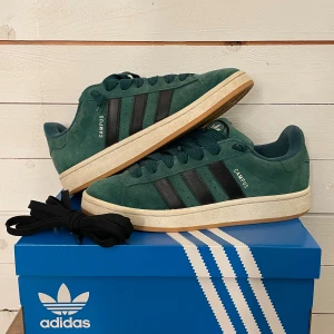 Adidas Campus gröna sneakers mocka - Tja! Säljer dessa Adidas Campus sneakers i mörkgrön mocka. Skorna har snörning och kommer med extra svarta skosnören. Skorna är sparsamt använda med ett slitage på insidan av ena skon, men det är inget som syns vid användning. Hör av dig vid minsta fundering!