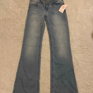 Bootcut jeans från Nelly med broderi - Snygga ljusblå bootcut jeans från Nelly med coolt rosa broderi på bakfickorna. Jeansen har låg midja, klassisk femficksdesign och dubbla knappar fram. Materialet är mjukt denim och passformen är loose med breda ben. Aldrig använda och prislappen sitter kvar.