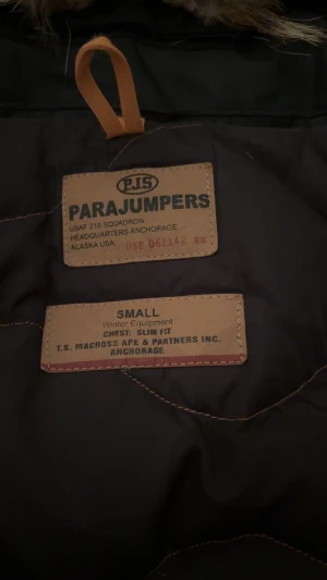 Svart Parajumpers vinterjacka med päls - Svart Parajumpers vinterjacka i slim fit med snygg päls på huvan, flera fickor och ikonisk patch på ärmen. Jackan har dragkedja, knappar och coola gula detaljer. Perfekt för kalla dagar när du vill hålla stilen. Pris kan även diskuteras 