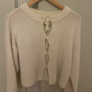 Beige stickad kofta med snörning - Supermysig beige stickad kofta med lång ärm och snygg snörning framtill. Koftan har en lite loose passform och är perfekt för att hålla sig varm under kyliga dagar. Ribbad struktur och mjukt material gör den extra skön att bära.