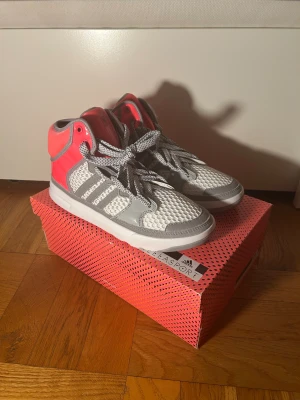 Adidas Stellasport sneakers high-top - Snygga Adidas Stellasport high-top sneakers i vitt, grått och neonrosa. Ovandel i mesh och syntet med gråa detaljer och klassiska Adidas-ränder. Skorna har snörning och platt sula, perfekt för dig som gillar sportig och färgstark stil. Strl 38, 38,5 och 40 finns i lager vid förfrågan