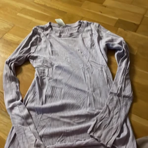 Ljuslila ribbad långärmad tröja Lindex - Säljer en ljuslila långärmad tröja från Lindex med ribbad struktur och broderad text 'life' med ett hjärta på bröstet. Tröjan är mjuk och har rund hals, perfekt för dig som gillar enkel men söt stil.