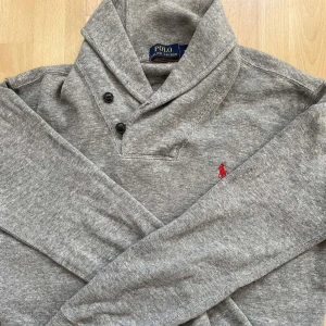 Ralph lauren hoodie - Säljer en stilren grå tröja från Polo Ralph Lauren med en liten röd logotyp på bröstet. Tröjan har en hög krage med knappar och långa ärmar. Perfekt för en avslappnad och snygg look. Strl M men kan passa S. Skick 10/10. Pris är diskuterbart🔥⭐️