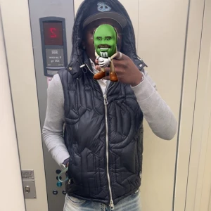 Svart dunväst med huva från Demont - Säljer en svart dunväst från Demont i storlek M. Västen har en quiltad design, dragkedja framtill och en stor huva. Materialet är glansigt och ger en alesäs mystisk vibe och passar med det mesta.