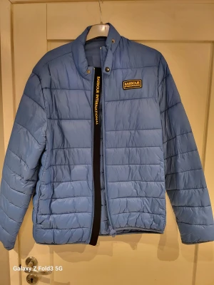 Ljusblå Barbour pufferjacka M - Säljer en ljusblå pufferjacka från Barbour International i storlek M. Jackan har quiltad design, ståkrage med tryckknapp och dragkedja framtill. Barbour-logga på bröstet och insidan. Perfekt för kyliga dagar och har en clean, modern look.