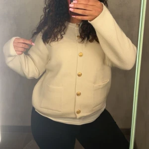 Beige kofta med guldknappar - Säljer en beige kofta med snygga guldknappar framtill och två praktiska fickor. Koftan har långärmad design och är tillverkad i ett stickat material som känns mjukt och skönt. Perfekt för dig som gillar klassisk och clean stil.