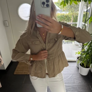 Beige kofta från Zara med volang - Säljer en beige overshirt från Zara i storlek XS. Jackan har volang nedtill, bröstfickor med knappar och långa ärmar med knappdetalj vid mudden. 