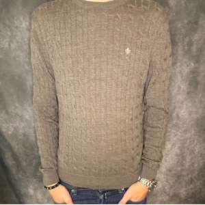 Brun stickad tröja Morris - Säljer en brun stickad tröja från Morris med diskret logga på bröstet. Tröjan har ett klassiskt kabelstickat mönster, rund halsringning och långa ärmar. Perfekt för dig som gillar stilrena och tidlösa plagg.