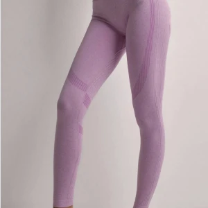 Ljuslila seamless leggings ICIW - Säljer ett par ljuslila seamless leggings med snygga ribbade detaljer och mönster längs benen. De är höga i midjan och har en tight passform som sitter skönt och följsamt. Perfekta för träning eller chill dagar.