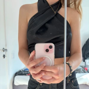 Svart halterneck topp - Svart halterneck topp i satin från nakd. Toppen har en öppen rygg och knyts i bak.