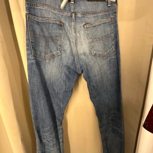 Tiger of Sweden ljusblå jeans - Ljusblå jeans från Tiger of Sweden med klassisk femficksdesign, kontrastsömmar och en cool patchdetalj på ena låret. Jeansen har normal passform och raka ben, tillverkade i bomullsdenim. Perfekta för dig som gillar en avslappnad men ändå stilren look.