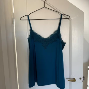 Turkos linnetopp med spets från New Yorker - Säljer en turkos linnetopp från New Yorker i storlek S. Toppen har tunna axelband och v-ringning med fina spetsdetaljer längs kanten. Perfekt för varma dagar eller att styla lager på lager. Materialet känns mjukt och lätt mot huden.🥰