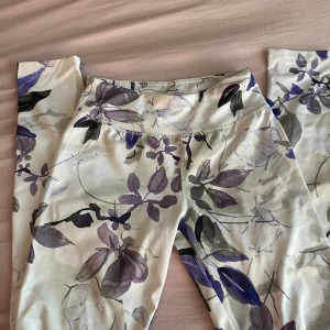 Blommiga leggings från SOC - Snygga leggings från SOC med blommigt mönster i lila, grått och svart på vit botten. De är stretchiga och sitter skönt med hög midja, perfekta för träning eller chill. Materialet är mjukt och följsamt syntet, så de är riktigt bekväma att ha på sig.