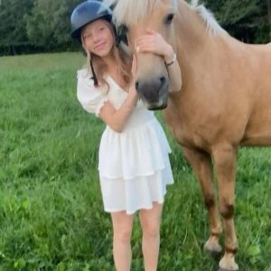 Vit kortklänning med volang - Supersöt vit kortklänning med volangkjol och puffiga kortärmar. Klänningen har en feminin v-ringning och dubbla lager i kjolen som ger extra volym. Perfekt för sommarens alla tillfällen och ger en romantisk vibe.