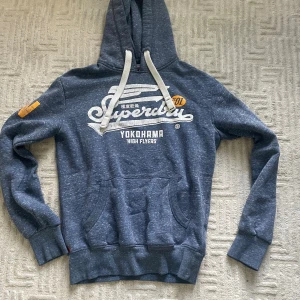 Blå superdry hoodie - Säljer nu denna Asfeta blå superdry hoodie i bra skick från superdry! Jättefin blå färg som är lätt att stylea och en perfekt varm hoodie inför vintern! Storlek S passar TTS. Vid fler frågor är det bara att skriva!