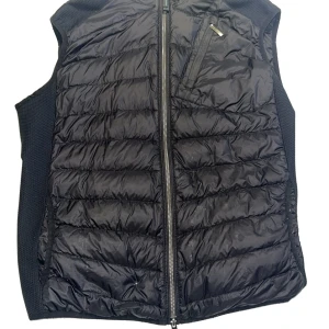 Svart dunväst från Parajumpers L - Snygg svart dunväst från Parajumpers i storlek L. Västen har quiltad framsida och baksida, dragkedja framtill och praktiska fickor med dragkedja. Perfekt för lager-på-lager och ger en sportig vibe till din outfit.