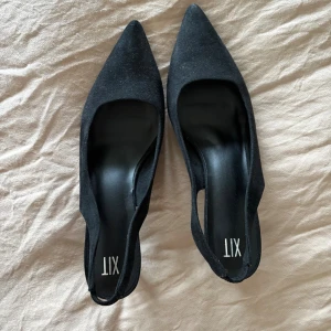 Svarta klackar med spetsig tå  - Snygga svarta pumps från XIT med spetsig tå och öppen häl. Skorna har en elegant låg klack och är tillverkade i mocka-liknande material. Perfekta för att lyfta din outfit med en stilren och modern touch. Aldrig använda
