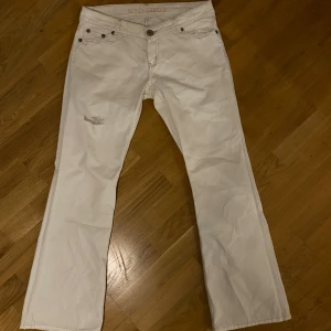 Vita jeansbyxor med bootcut - Snygga vita jeans från River island med bootcut passform. Byxorna har klassiska fem fickor, slitningar fram och bak samt detaljer i silverfärgade nitar. Tillverkade i mjukt jeanstyg som ger en avslappnad vibe.