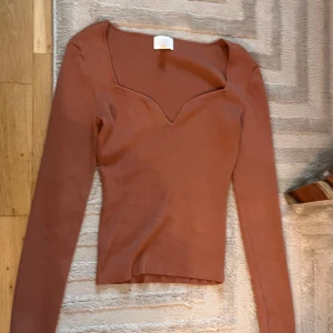 Brun ribbad långärmad topp - Säljer en brun ribbad långärmad topp med snygg v-ringad hals. Modellen är figurnära och har en mjuk, stretchig känsla som gör den skön att bära. Perfekt att styla med jeans eller kjol för en chill look.