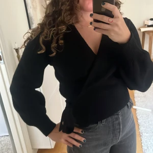 &Other Stories Svart omlottkofta - Svart omlottkofta från & Other Stories med knyt i sidan och v-ringning. Koftan har långa ärmar och är tillverkad i en mjuk mix av akryl, polyamid, ull och elastan. Perfekt för lager-på-lager och snygg till både jeans och kjol. Lite nopprig men kan fixas med bopped borttagare. Mkt kvar att ge. 