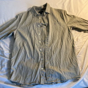 Lusgrön skjorta från GANT, 170 cm - Snygg beige skjorta från GANT med klassisk krage och broderad logga på bröstet. Skjortan har lång ärm, knäppning framtill och är gjord i bomull. Perfekt för en clean och stilren look. Modellen på bilden. 180. Då den passar perfekt för personer runt 170-175 cm.