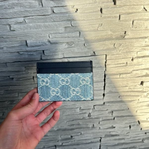 Gucci blå korthållare i denim och skinn - Snygg korthållare från Gucci i blå denim med klassiskt GG-mönster och svarta skinnkanter. Perfekt för dig som vill ha en stilren och lyxig accessoar till dina kort. Smidig och lätt att ta med i fickan. Såklart äkta!