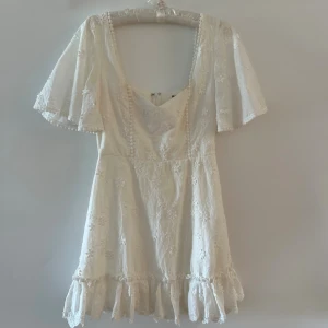 Vit blommig kortklänning från Showpo - Superfin vit kortklänning från Showpo med broderade blommor, volangkant nertill och vida korta ärmar. Använd 1 gång. Perfekt för studenten.