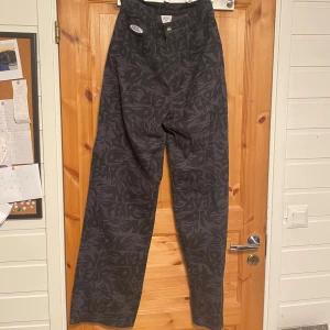 Svarta wide byxor med mönster frår en collab mellan H&M och No Fear  - Snygga svarta byxor från No Rules med mörkgrått grafiskt mönster. Modellen är wide och högmidjad med raka ben och klassisk knappgylf. Byxorna har cool streetkänsla och är tillverkade i bomullsmix. Perfekta för dig som vill sticka ut med en unik look.