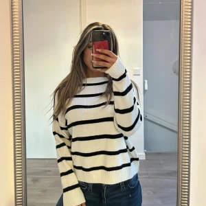 Vit och svart randig stickad tröja - Vit stickad tröja med svarta horisontella ränder och rund hals. Tröjan har en relaxed fit och långa ärmar, perfekt för lager-på-lager under kyligare dagar. Mjuk och skön känsla, passar till jeans eller kjol.