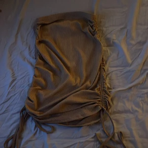 Beige/brun ribbad kjol med snörning - Säljer en beige/brun ribbad kjol med snygga snörningsdetaljer på sidorna. Kjolen har ett figurnära passform och är gjord i ett mjukt, stretchigt material som sitter skönt. 