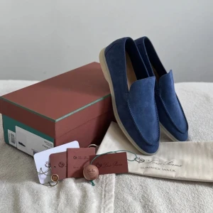 Blå mockaloafers från Loro Piana - Snygga loafers från Loro Piana i marinblå mocka med ljus sula. Modellen Summer Walk har en stilren design med rund tå och platt sula, perfekt för en clean och avslappnad look. Skorna är tillverkade i Italien och kommer med lkartong och dustbag.