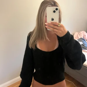 Svart stickad tröja med djup ringning - Mysig svart tröja med mjuk känsla och djup, rundad ringning. Tröjan har långa ärmar och en lite loose passform, perfekt för dig som gillar en enkel men ändå trendig look. Världens skönaste material 