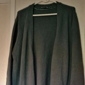 Mörkgrön stickad kofta - Mysig mörkgrön stickad kofta.. Koftan är öppen framtill, har lång ärm och två fickor. Den är lite nopprig. Perfekt att slänga på sig när det är kyligt ute. 