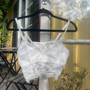 Vit spetsig croppad linnetopp - Säljer en vit croppad linnetopp från nelly i spets med tunna axelband och v-ringning. Toppen har fina spetsdetaljer och en lätt fransig kant nertill. Perfekt för sommarens varma dagar🌸