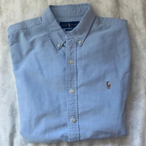 Blå skjorta från Ralph Lauren Slim Fit - Klassisk ljusblå skjorta från Ralph Lauren i slim fit-modell. Skicket på skjortan är sjukt bra, endast etiketten som är lite sliten. Kontakta vid funderingar🙌