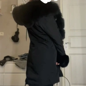 Julia parkasjacka lång svart äkta päls  - Snygg lång svart parkasjacka med fluffig päls runt huva, ärmslut och framkant. Jackan har en loose passform och stora fickor. Perfekt för kalla dagar med sin varma och lyxiga look. Stängs med knappar. !!äkta päls!! PRIS GÅR ATT DISKUTERA. Hör av dig för bilder på detaljer mm. 