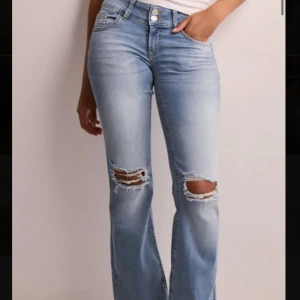 Ljusblå bootcut jeans med slitningar - Snygga ljusblå jeans med bootcut passform och slitna hål över knäna. Klassisk femficksmodell med dubbla knappar och dragkedja framtill. Bakfickor med lock och knappdetalj. Perfekta för en avslappnad och trendig look.