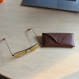 Ray-Ban aviator polarized glasögon med gul ton - Snygga Ray-Ban aviator-glasögon med tunna svarta metallbågar och stora gula glas. Klassisk pilotform som ger en cool vibe. Kommer med original brunt fodral med Ray-Ban-logga. Perfekta för dig som vill sticka ut med stil. Polarized