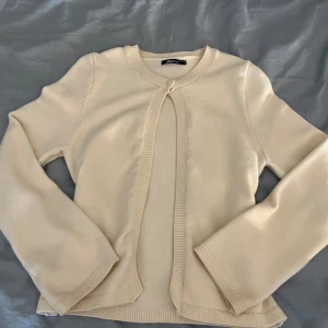 Vit kofta från Gina Tricot - Snygg vit kofta från Gina Tricot med ribbade kanter. Koftan har långärmad passform och stängs med en liten knapp upptill. Perfekt att slänga över en topp för en clean look.