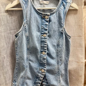 Ljusblå jeansväst från Gina Tricot - Snygg ljusblå jeansväst  med klassisk rund halsringning och knäppning framtill med silverfärgade knappar. Västen har figurnära passform och är tillverkad i robust denim. Väldigt snygg för en kväll ute på restaurang eller en utekväll med vännerna🤞🏻💕