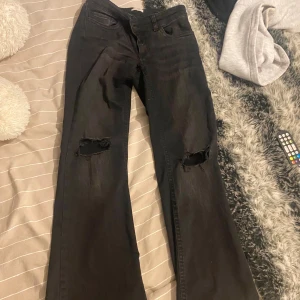 Svarta bootcut jeans med slitna knän - Svarta jeans från Nelly med bootcut passform och slitna hål på båda knäna. Klassiska femficksjeans med Nudie-signatur på bakfickorna. Knappt använd! 