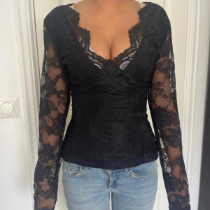 Svart spetsblus med v-ringning - Säljer en svart blus i spets med djup v-ringning och långa ärmar. .
