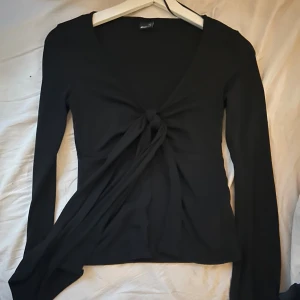 omlottopp Gina Tricot - Svart långärmad omlottopp från Gina Tricot med djup v-ringning och knyt framtill. Toppen har croppad passform och är tillverkad i ett mjukt, stretchigt material som sitter snyggt på kroppen. Perfekt för att skapa en trendig och stilren look. Max använd 2 gånger. Säljer pga att jag inte får någon användning av den.