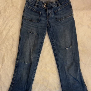 Blå jeans med slitningar och stora fickor - Snygga blå jeans från 157 med raka ben, slitna detaljer på låren och knäna samt stora framfickor. Jeansen har klassisk femficksdesign och dubbla knappar i midjan. Perfekta för en avslappnad och trendig look. Hålen på jeansen har jag gjort själv dom är väldigt lika jeansen i Gina! 
